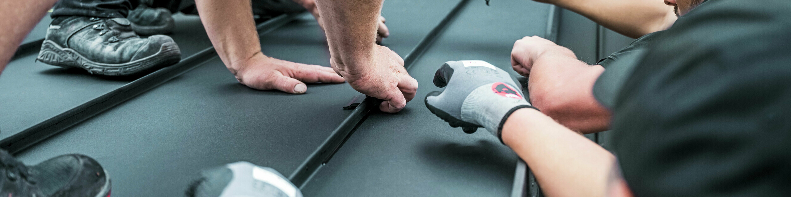 Mehrere Handwerker montieren gemeinsam auf einem PREFALZ Dach die Klemmen, um die Solarmodule verlegen zu können. 