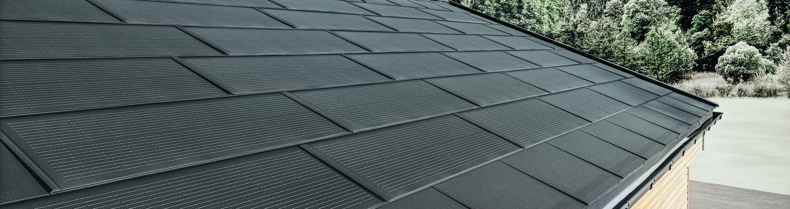 PREFA Solardachplatte in großer Ausführung kombiniert mit der Dachplatte R.16 in Schwarz, Kastenrinne und Lärchenholz-Fassade