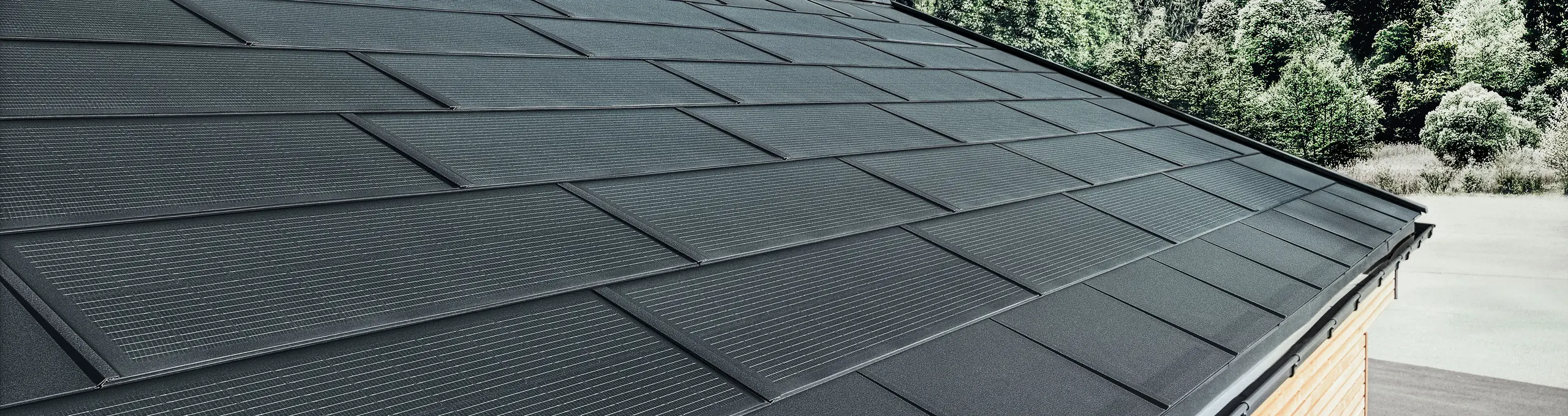 PREFA Solardachplatte in großer Ausführung kombiniert mit der Dachplatte R.16 in Schwarz, Kastenrinne und Lärchenholz-Fassade
